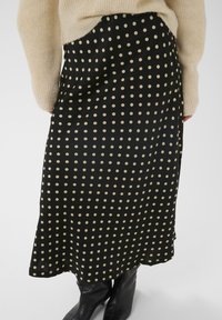 Jupe noire à pois en tissu lisse, avec de grands pois couleur crème et une coupe décontractée, associée à des bottes noires montantes.