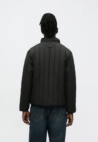 Gesteppte schwarze Jacke mit hohem Kragen, vertikalen Nähten und langen Ärmeln. Entworfen mit einer lockeren Passform und einfarbigem Design.
