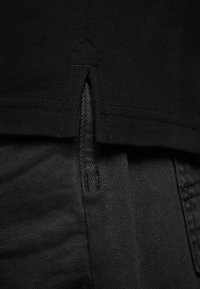 Tessuto nero con un design a maglia testurizzata e denim liscio. Presenta uno spacco sul fondo con cuciture visibili e un dettaglio con zip.