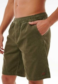 Olijfgroene corduroy shorts met een elastische tailleband, zijzakken en een klein bruin logo-label op de onderrand.