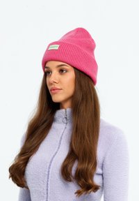 Roze gebreide beanie met ribbeltextuur en een klein label. Gekocht met een lichtpaarse ritstrui met een fuzzy textuur.