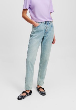 Vaqueros de mezclilla azul claro de pierna recta con cinco bolsillos, cierre de botón y un corte holgado, combinados con una blusa de mangas cortas color lavanda y zapatos negros con lunares.