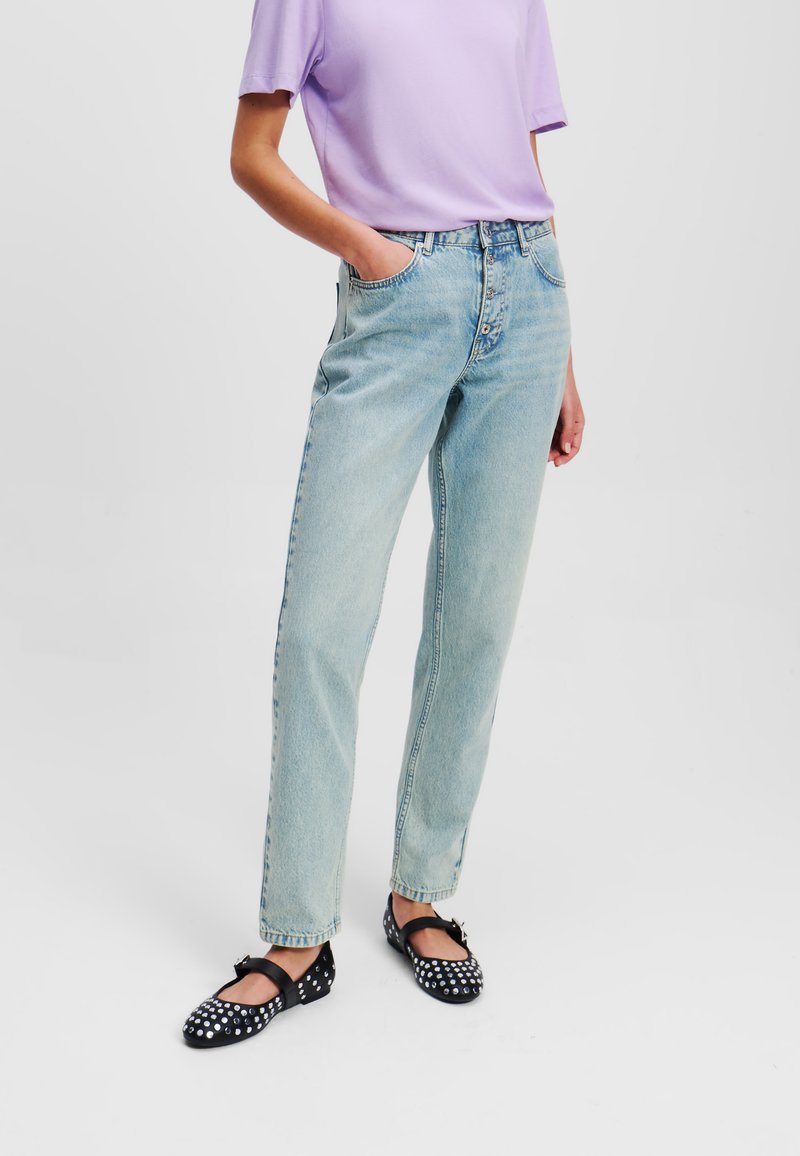 Lichtblauwe denim straight-leg jeans met vijf zakken, een knoopsluiting en een losse fit, gecombineerd met een kortmaya lavendeltop en zwarte schoenen met stippen.