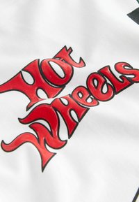 Un tessuto bianco presenta un audace logo "Hot Wheels" in rosso e nero, lucido e con un design simile a fiamme, ben in evidenza al centro.