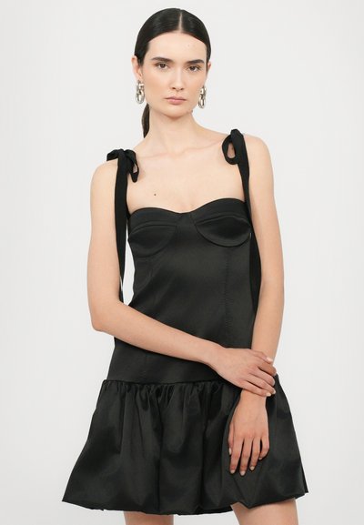 Vestido de satén negro con un cuerpo ajustado y un dobladillo con volantes, que presenta tirantes con lazo ajustables y un escote corazón. Textura suave en toda su superficie.