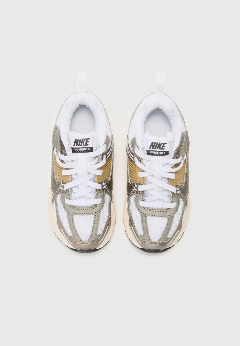Baskets Nike Vomero 5 avec une tige en mesh et synthétique, arborant des couleurs blanche, dorée et grise. Lacets épais blancs et un col rembourré.