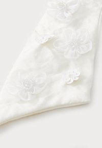 Fehér szövet kiegészítő, rétegezett virágdíszekkel, gyöngyökkel és flitterekkel. Az sima textúra és a hegyes forma fokozza a dizájnt.