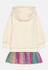 Hoodie crème avec un ourlet froncé orné de sequins colorés présentant des rayures verticales en rose, vert, or et bleu. Capuche et détails des poignets en tissu doux.