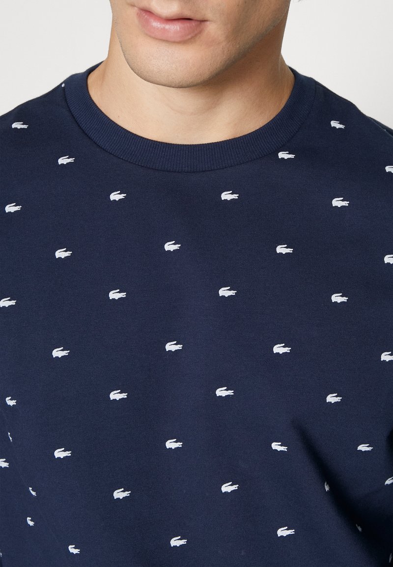 Marineblaue Sweatshirts mit Rundhalsausschnitt und verstreuten kleinen weißen Krokodil-Logos. Der Stoff wirkt weich und hat eine glatte Textur.