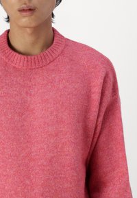 Pink knitted sweater with a ribbed crew neckline, featuring a soft texture and a slightly loose fit. No visible patterns or accents.
