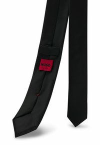 Schwarze Seidenkrawatte mit glatter Textur, versehen mit einem roten HUGO-Label und einem kleinen roten Akzentstich. Klassisches Design mit spitzem Ende.