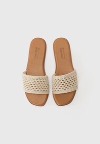 Sandali beige open-toe con una cintura intrecciata texturizzata e una soletta in pelle sintetica marrone liscia, caratterizzati da suole di forma quadrata.