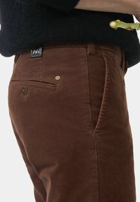 Pantalons en velours côtelé marron avec une texture lisse, dotés d'une poche arrière, d'accents en métal et d'une étiquette tissée près de la taille.