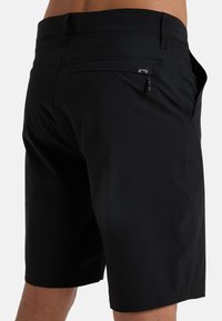Černé šortky vyrobené z lehkého materiálu, s kapsou na zip na zadní straně, poutky na pásek a čistým, přizpůsobeným střihem.