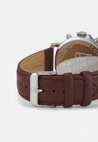 Bracelet de montre en cuir marron avec boucle en métal argenté, présentant des détails de couture et des trous d'ajustement pour un ajustement de taille.