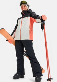 Smučarska jakna v črni in koralni barvi z zadrgo spredaj, kombinirana s črnimi smučarskimi hlačami. Dodatki vključujejo smuči in palice, vidna so tudi očala in rokavice.