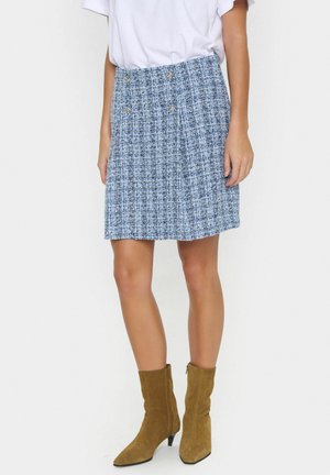 En blå tweedkjol med plisserad design, prydd med två dekorativa knappar i midjan, kombinerad med tanfärgade mocka ankle boots.