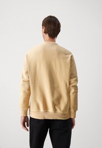 Felpa gialla in cotone con maniche lunghe, polsini e orlo a costine. Presenta un colletto a girocollo. Design semplice e privo di decorazioni. Pantaloni scuri visibili.