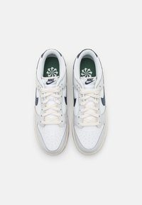 Sneakers bianchi in pelle con accenti blu navy, punta perforata e lacci crema. Soletta verde con un design floreale, logo Nike sul lato.
