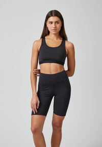 Zwart sportoutfit met een getailleerde sportbeha en hoge shorts, gemaakt van een glad, rekbaar materiaal zonder zichtbare patronen.