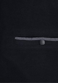 Tessuto nero a costine con una tasca orizzontale caratterizzata da una fodera a righe grigie e una chiusura con bottone nero.