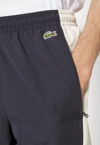 Tmavě modré a krémové kraťasy s elastickým pasem, boční kapsou, strukturovanou látkou a malým zeleným krokodýlkem jako logem.