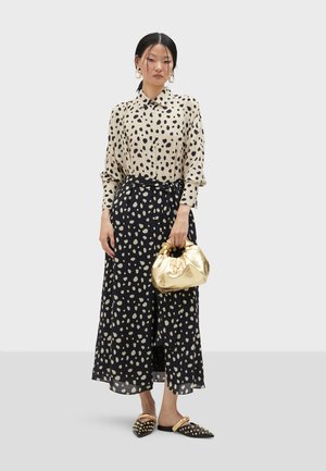 Beige polka-dot blouse, black skirt with cream spots, gold bag, and studded black mules. Lightweight fabric, relaxed fit, and knotted belt.