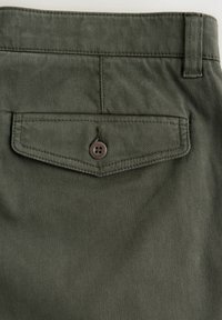 Close-up of olive green fabric trousers showing a buttoned flap back pocket and belt loop.