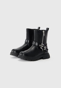 Bottes noires en cuir jusqu'à la cheville avec une fermeture éclair sur le côté, des détails de boucle et une semelle en caoutchouc texturée. Comprend des languettes pour un enfilage facile.