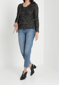 Czarny i biały sweter o fakturze z dekoltem w serek, niebieskie dżinsy i czarne botki na obcasie. Prosta torebka w ręku.