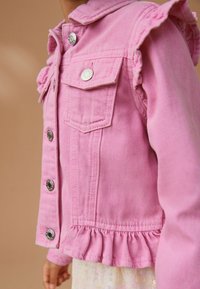 Veste en denim rose avec des accents de manches froncées, boutons en métal argenté et un ourlet à volants. Deux poches avant et tissu texturé.