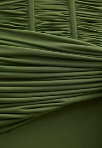 Κοντινή λήψη σε ύφασμα ελιάς με οριζόντιες και κάθετες πτυχές που δημιουργούν μια ρυτιδιασμένη, επίπεδη υφή.