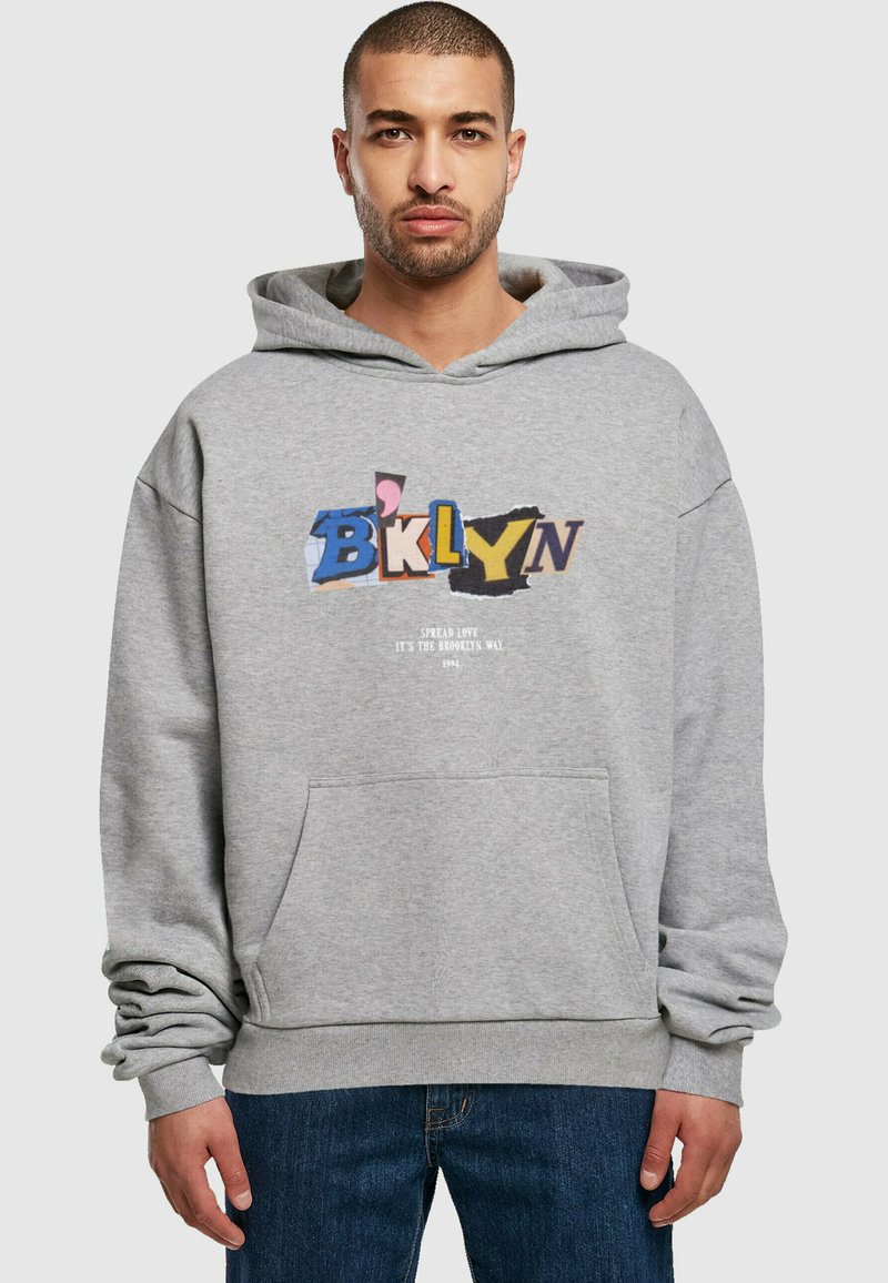 Sudadera gris con un bolsillo delantero, que presenta un gráfico colorido de "BKLYN" y el texto "Spread Love It's the Brooklyn Way" debajo. Material suave.