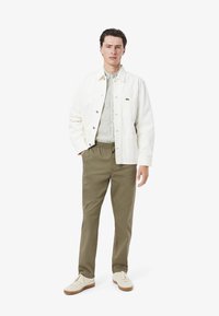 Witte katoenen jas met zilveren knopen, gecombineerd met een gestreept shirt en olijfgroene broek met koordjes. Crème sneakers met bruine zolen.