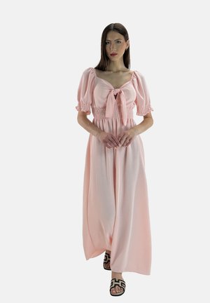 Abito maxi rosa con maniche a sbuffo, vita arricciata e un fiocco davanti. Tessuto morbido con una silhouette fluida. Indossato con sandali neri.