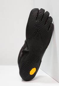 Schwarzer Fünf-Finger-Schuh mit strukturiertem Gummisohlenprofil und gelbem Vibram-Logo. Obermaterial aus Wildleder mit glatter, flexibler Oberfläche.