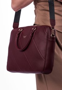 Burgunderfarbene Ledertasche mit diagonaler Steppnaht, zwei oberen Tragegriffen, abnehmbarem Tragegurt und goldenen Hardware-Details.