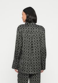 Čierna košeľa s geometrickým vzorom, s dlhými rukávmi, golierom a rovnostrih. Hladká textúra a zapínanie na gombíky vzadu.