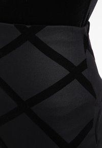 Musta ja tummanharmaa kangas, jossa on suuri samettinen vino ruutukuvio ja sileä pinta sovitetussa vaatteessa.