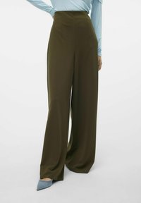 Höga vida byxor i mörk olivgrön, tillverkade av slät tyg med en ren finish. Kombineras med en ljusblå långärmad topp.