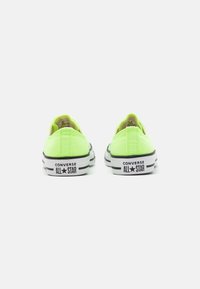 Un paio di sneakers Converse All Star low-top di colore verde neon viste da dietro, con il logo "CONVERSE ALL STAR" sui bordi della suola bianca.