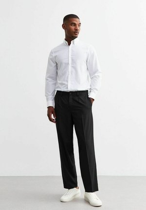 Witte button-down shirt gecombineerd met zwarte broek en witte sneakers. Het shirt heeft een klassieke kraag en de broek is recht gesneden.
