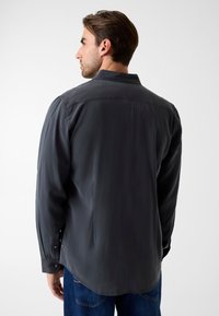 Grijs shirt met lange mouwen, klassieke kraag, gladde textuur en knoopmanchetten. Heeft een rechte zoom en subtiele zijsplitten.