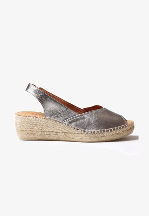 Sandalia cuña esparto con talón descubierto de cuero plateado, punta cerrada y suela trenzada de yute sobre fondo blanco.