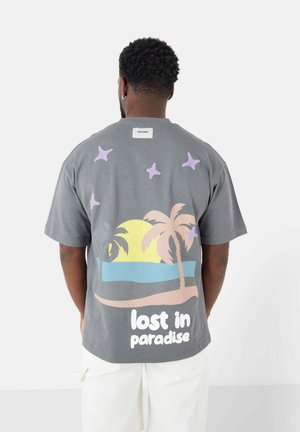 Grijze T-shirt met een kleurrijke strandscène met palmbomen en de tekst "verloren in het paradijs" op de achterkant. Korte mouwen en een ontspannen pasvorm.