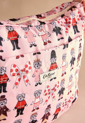 Pehmeä pussi vaaleanpunaisesta kankaasta, jossa on toistuvia kuvioita leikkisistä karhuista eri asuissa, pilkkuja ja "Cath Kidston" -etiketti.