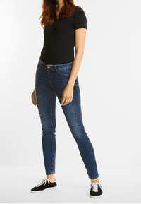 Jeans ajustados azules de mezclilla, con cinco bolsillos y un ligero desgaste. Combinados con una camiseta negra y zapatillas negras con cordones.