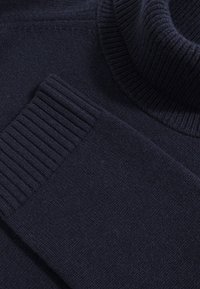 Pull en laine bleu marine foncé à col roulé tricoté avec poignets et détails de col côtelés, étalé à plat.