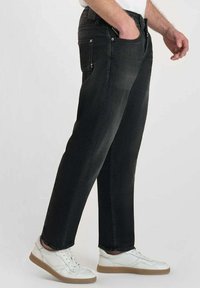 Jean en denim noir avec une coupe droite, poches avant et fermeture à boutons. Portés avec des baskets blanches à semelle beige.