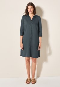 Abito camicia di colore grigio scuro, realizzato in tessuto morbido, con colletto, maniche a tre quarti e spacchi laterali all'orlo.